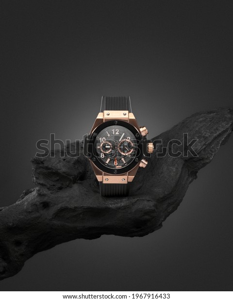 Beautiful gold men\'s watch with a black strap on a\
wooden stand, on a gray background. Beautiful gold watch. A luxury\
brand watch