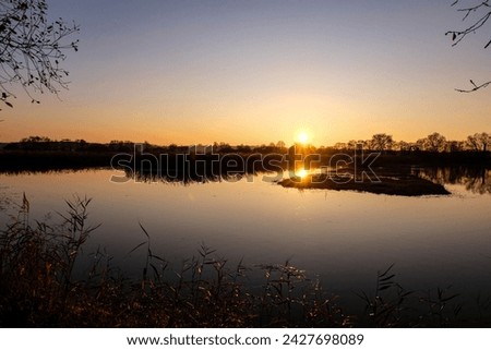 Beautiful golden sunset with reflection over calm, placid lake in the rural countryside of Somerset Levels in England, UK