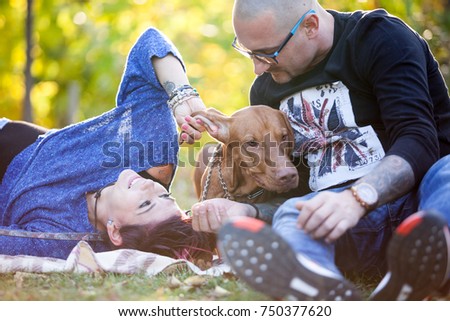Beautiful gorgeous family of three playing in the park with their dog while lying on the grass. Animal lovers. Mother, father, daughter and their dog