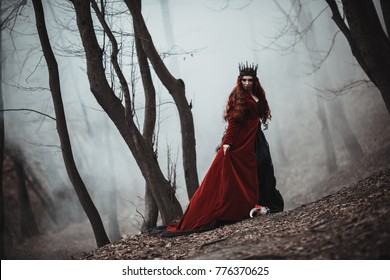 Beautiful gothic queen in red dress doing magic in the autumn forest 