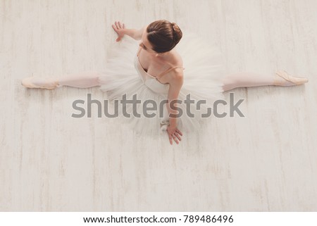 Beautiful graceful ballerina in pointe shoes at white wooden floor makes ballet leg stretching. Ballet practice of classical dancer doing splits, copy space