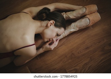 Beautiful Graceful Young Ballerina In Pointe Shoes Dancing On The Brown Wooden Floor Background. Female Stretching Indoors Toes Professional Arts. Back Of Ballet Dancer. Top View From Above Copy Space