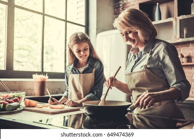 Beautiful grandma and granddaughter are talking and smiling while cooking in kitchen