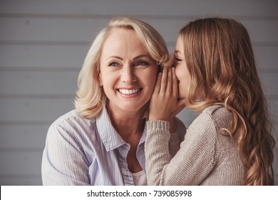 Beautiful granny is smiling while teenage granddaughter is whispering her something