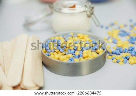 Beautiful granules of pink, white, yellow, blue wax for depilation in a glass bowl, wooden spatulas on a pink background. waxing. Epilation, depilation, removal of unwanted hair.