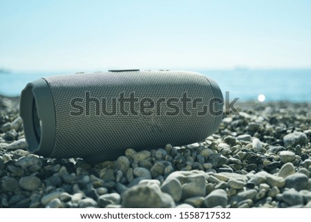 Beautiful gray portable speaker in the fresh air on the beach on the background of sea pebbles. Direct sunlight