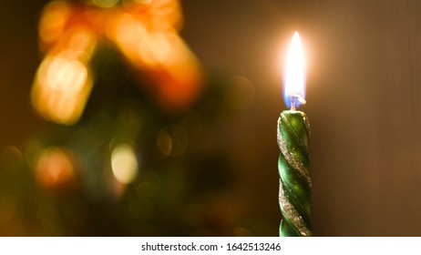 Beautiful Green Candle Burning On A Christmas Eve With The Decorated Blurred Christmas Tree On The Background. Concept. Burning New Year Candle, Time Lapse Effect.