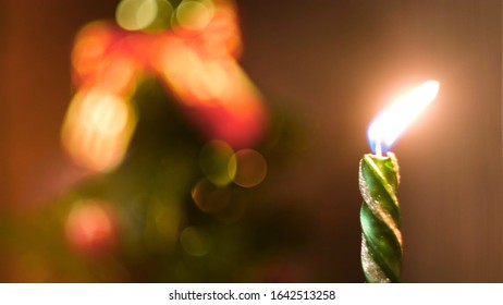 Beautiful Green Candle Burning On A Christmas Eve With The Decorated Blurred Christmas Tree On The Background. Concept. Burning New Year Candle, Time Lapse Effect.