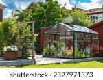 Beautiful greenhouse glass house in the garden yard near the villa. Wicker rattan chairs inside. Lots of pots with different plants.  Greenhouse for growing plant seedlings. Landscape garden design.