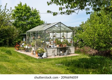 Beautiful greenhouse glass house in the garden yard near the villa. There are lots of pots with blooming blossom colorful flowers. Landscape garden design. Greenhouse for growing plant seedlings. - Shutterstock ID 2096696059