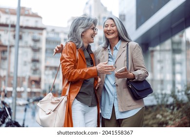 Beautiful Grey Haired Senior Women Companions On Modern City Street At Walking On Nice Autumn Day. Friends Spend Time Together