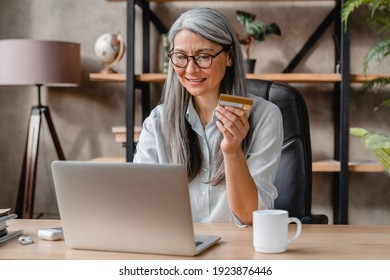 Beautiful Grey-haired Mature Woman Doing Online Shopping With Credit Card And Laptop In Office
