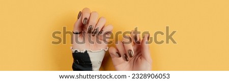 Beautiful groomed womans hands with brown nail design on yellow background
