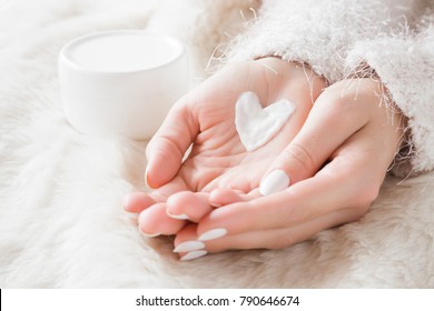 
Beautiful groomed woman's hands with cream jar on the fluffy blanket. Moisturizing cream for clean and soft skin in winter time. Heart shape created from cream. Love a body. Healthcare concept. 