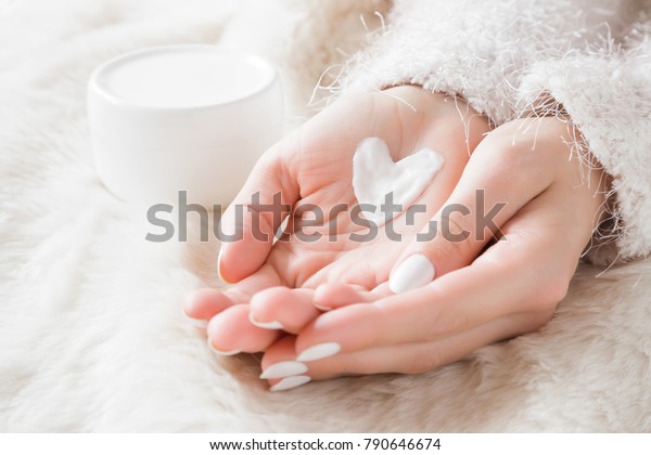 \
Beautiful groomed woman\'s hands with cream jar on the\
fluffy blanket. Moisturizing cream for clean and soft skin in\
winter time. Heart shape created from cream. Love a body.\
Healthcare concept.\
