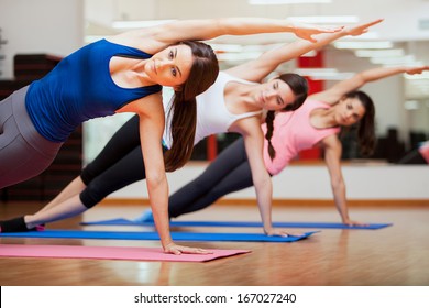 Beautiful group of women practicing the side plank yoga pose during a class in a gym