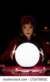 Beautiful Gypsy Fortune Teller Woman Looking At Magic Crystal Ball For Predict Future With Her Hands Around. Divine Magic, Forecast Esoteric Astrology Supernaturalism, Magical Power, Alchemy.