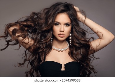 Schönes Haar. Modefrau mit Perlen. Brunette-Modell mit Make-up und Wavy Frisur-Haltung im Studio. Porträt eines schönen Mädchens mit Schmuck einzeln auf schwarzem Hintergrund.