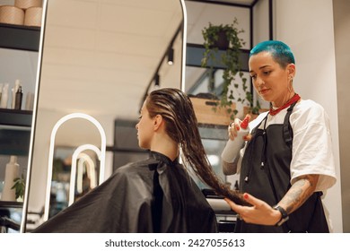 Beautiful hair stylist with tattooed hands applying spray on woman wet hair in beauty salon - Powered by Shutterstock