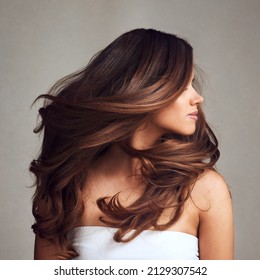 Haciendo historia de cabello todos los días con un hermoso cabello. Imagen de estudio de una joven hermosa mujer con el largo y hermoso cabello posando sobre un fondo gris.