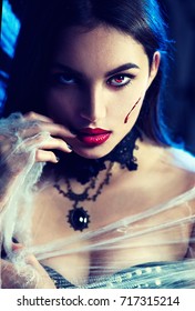Beautiful Halloween Vampire Woman portrait. Beauty Angry Sexy Vampire Witch lady with blood on mouth posing in darkness, wearing spider web. Art design. Mysterious Model girl with Halloween make up