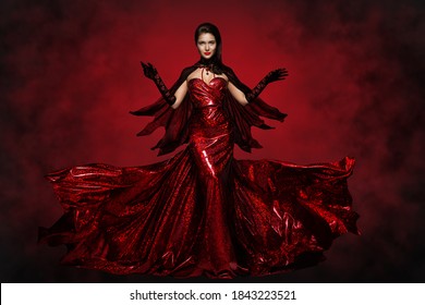 Beautiful Halloween Witch in Red Dress, Gloves and Cape, Gothic Fashion Girl Raised Open Arms, making Magic Witchcraft. Spooky Dark Smoke Background