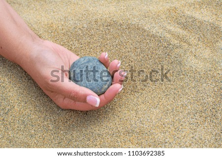 Beautiful hand holding a stone, on a beach sand background.