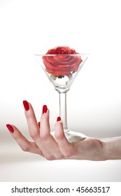 Beautiful hand with perfect red manicure holding martini glass with red rose inside. youth and beauty concept