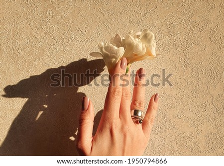 Beautiful hand young girl with manicure. Finger take a flowers. Hard light on top background.