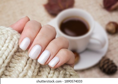 Beautiful hand of a young woman with a knitted sweater and autumn leaves. The nails are covered with a white gel Polish with a shimmer. Manicure ideas.