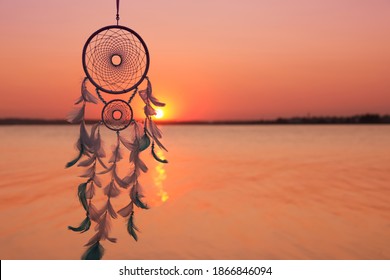 Beautiful handmade dream catcher near river at sunset. Space for text