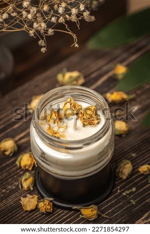 Beautiful handmade fragrant candle with yellow flower buds in a glass jar on the wooden background.