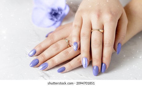 Beautiful hands with fresh violet manicure holding orchid flower and lying on a white table. Spa or wellness holiday winter banner. Trendy color 2022 Very Peri manicure