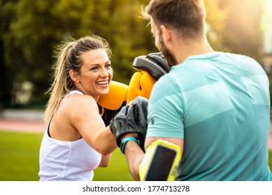 Beautiful handsome healthy young woman sparring and laughing with a boxing partner outdoors. Couple in park boxing. - Powered by Shutterstock