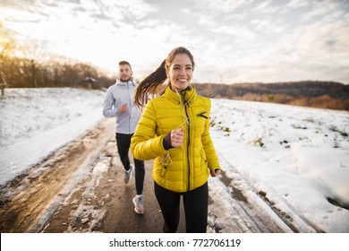 Beautiful happy active runner girl jogging with her personal handsome trainer on a snowy road in nature. - Shutterstock ID 772706119