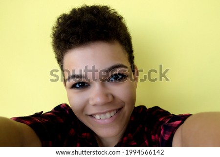 beautiful and happy African American woman with short hair on a yellow background, takes a selfie, close-up portrait.