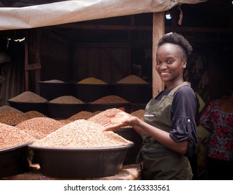 A Beautiful And Happy African Nigerian Female Trader, Seller, Business Woman Or Shop Owner Preparing To Sell Goods To Her Customers In A Market