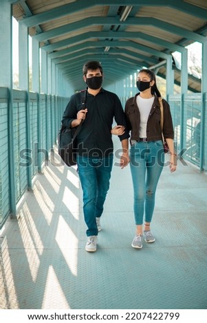 Beautiful, happy Asian, Indian young couple holding hand of each other and walking on flyover across. They are wearing a protective face mask in covid 19 pandemic.  