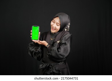 Beautiful Happy Asian Muslim Girl Pointing At Green Screen Phone On Black Background