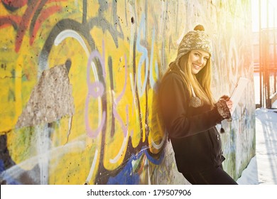 Beautiful happy blonde Caucasian teenage girl using tablet computer. Cute teenager with tablet pc against graffiti wall outdoors in winter. Technology and modern lifestyle. - Powered by Shutterstock