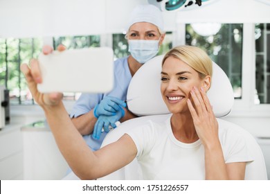Beautiful and happy blonde woman at beauty medical clinic. She is sitting and talking with female doctor about face esthetics treatment. - Powered by Shutterstock