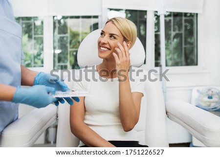 Beautiful and happy blonde woman at beauty medical clinic. She is sitting and talking with female doctor about face esthetics treatment.