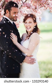 Beautiful Happy Bride And Groom Being Showered With Confetti From Cherry Blossoms