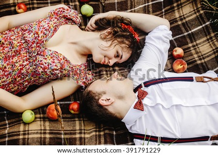 beautiful happy bride and stylish retro groom lying on tweed blanket, cuddling and  relaxing, picnic in sunny meadow