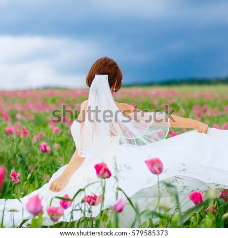 Beautiful happy bride in white dress  having fun in flower poppy field on summer day. Just married, young amazing woman.