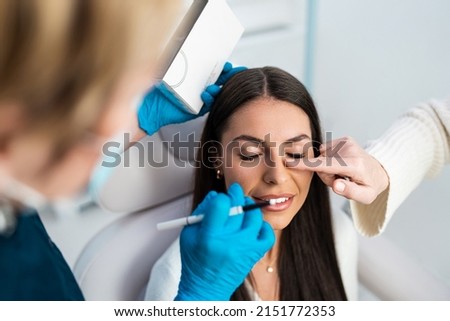 Beautiful and happy brunette woman at beauty medical clinic. She is sitting and talking with two female doctors about face aesthetic treatment.