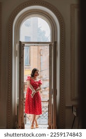 a beautiful and happy brunette women in red retro dress and gloved in the balcony doorway . the concept of the stylist's work. thematic photo shoot. - Shutterstock ID 2259174843