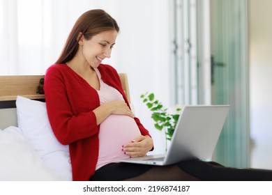 A Beautiful, Happy Caucasian Mother Sits In Bed Using Her Laptop Computer To Search For Information. The New Mother Uses The Laptop To Work And Relax At Home.