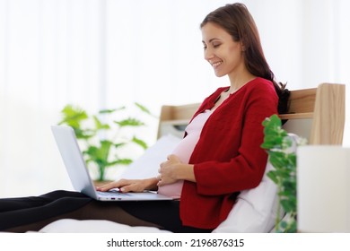 A Beautiful, Happy Caucasian Mother Sits In Bed Using Her Laptop Computer To Search For Information. The New Mother Uses The Laptop To Work And Relax At Home.