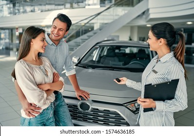 Beautiful happy couple bought a car in the dealership and receives the keys from the manager.